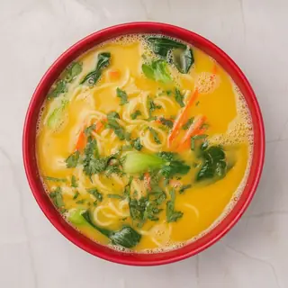 Steaming bowl of Himalayan chicken thukpa noodle soup with fresh vegetables and herbs